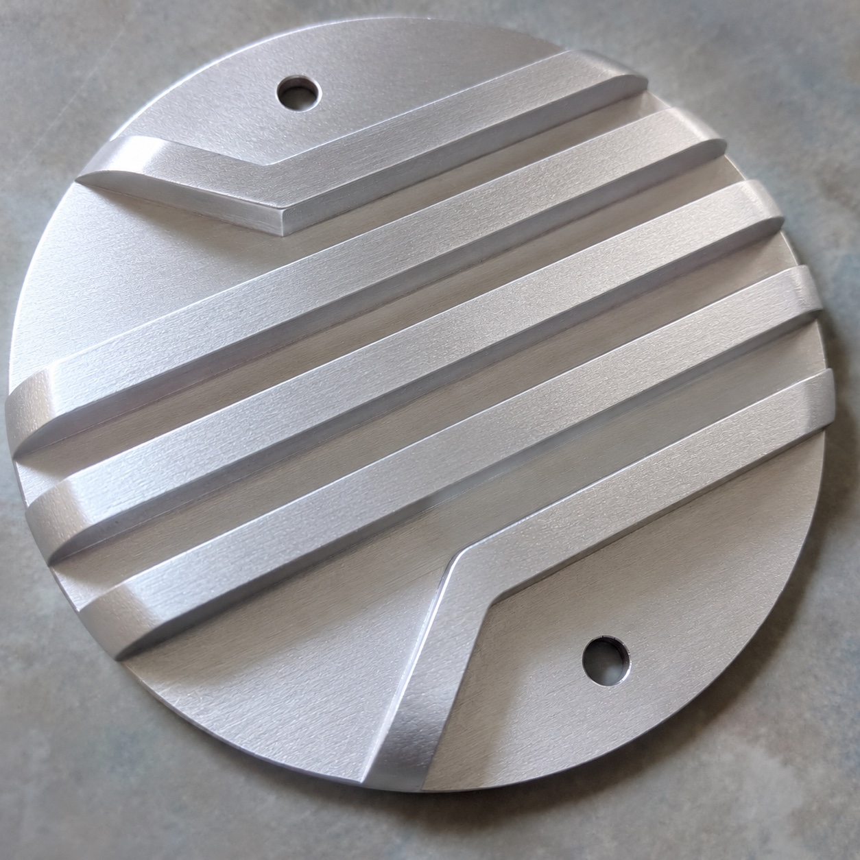 A handmade round motorcycle points cover with raised diagonal fins and two mounting holes
